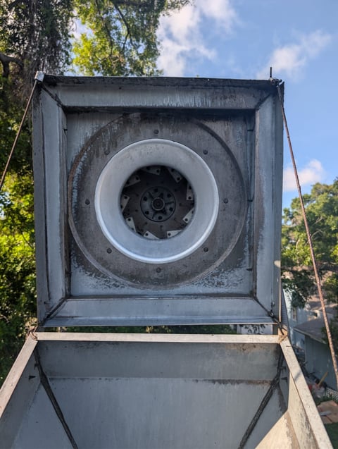 Interior view of a large industrial fan mounted inside a metal duct with trees and blue sky visible in background