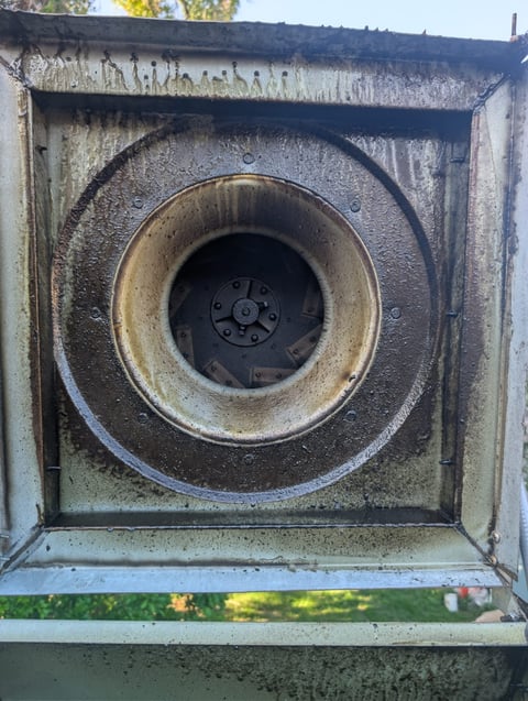 Close-up of a weathered metal dryer vent showing rust and debris accumulation around the circular opening