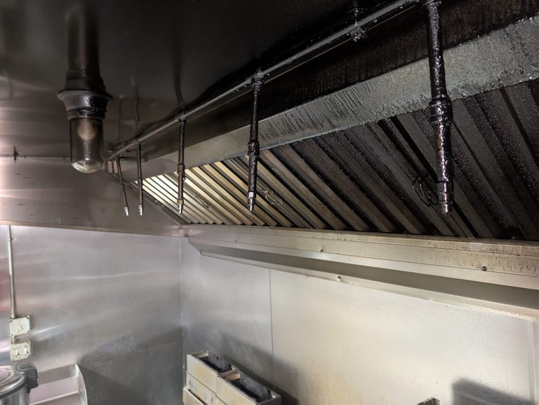 Interior of commercial kitchen with stainless steel hood vents and metal piping system mounted above a prep area