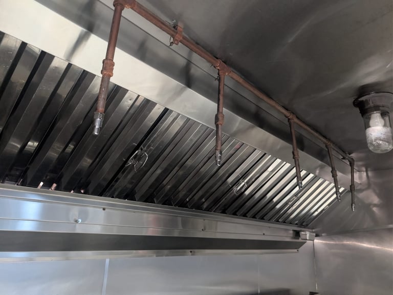 Industrial kitchen hood ventilation system with stainless steel ductwork and overhead exhaust grilles mounted on ceiling